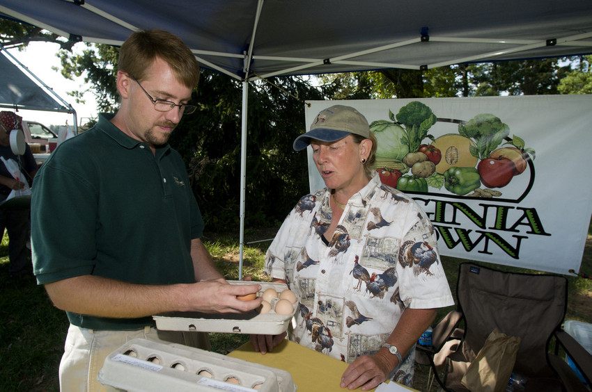 A vendor at a farmers market speaks with a customer about locally grown eggs.