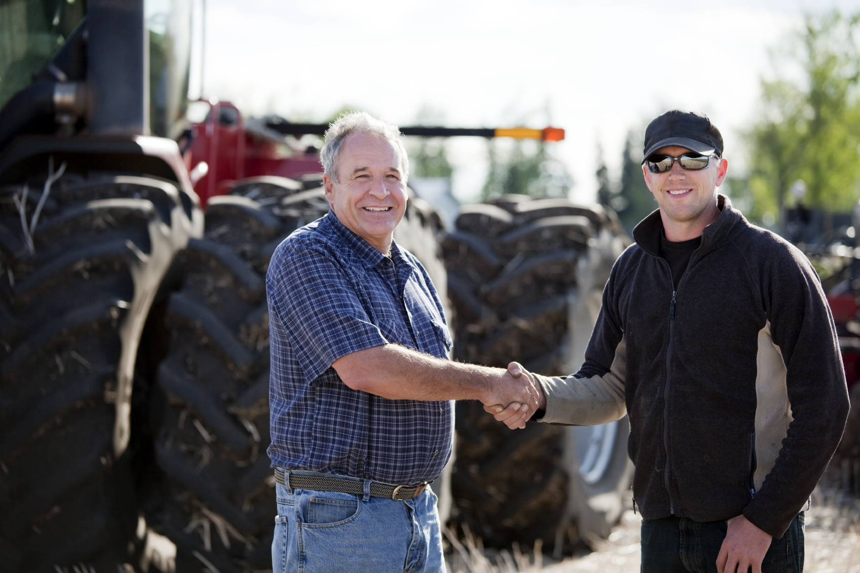 Older man shakes hands with younger man. Tractor in background.