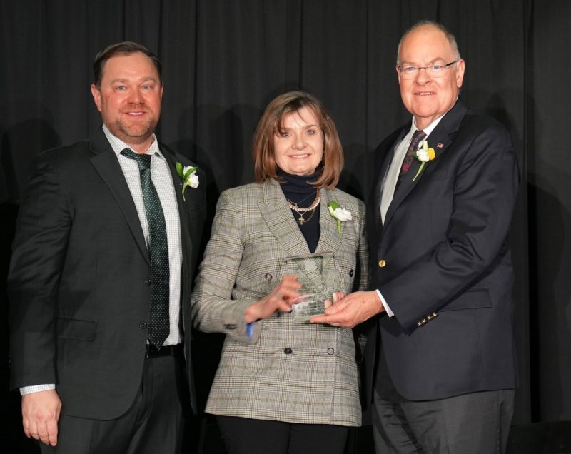 Three people pose, holding a glass award.