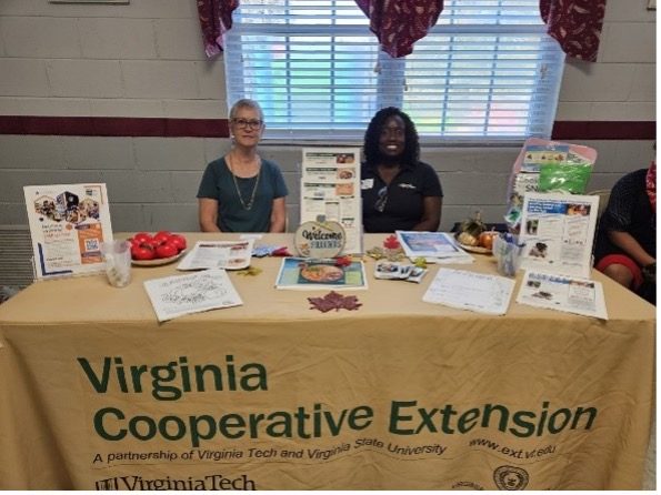 two people sitting at a table, tan Virginia Cooperative Extension table cloth and brochures on the table