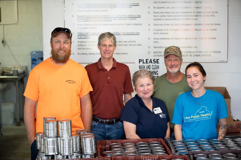 Group of people pose behind a table laden with silver metal cans.