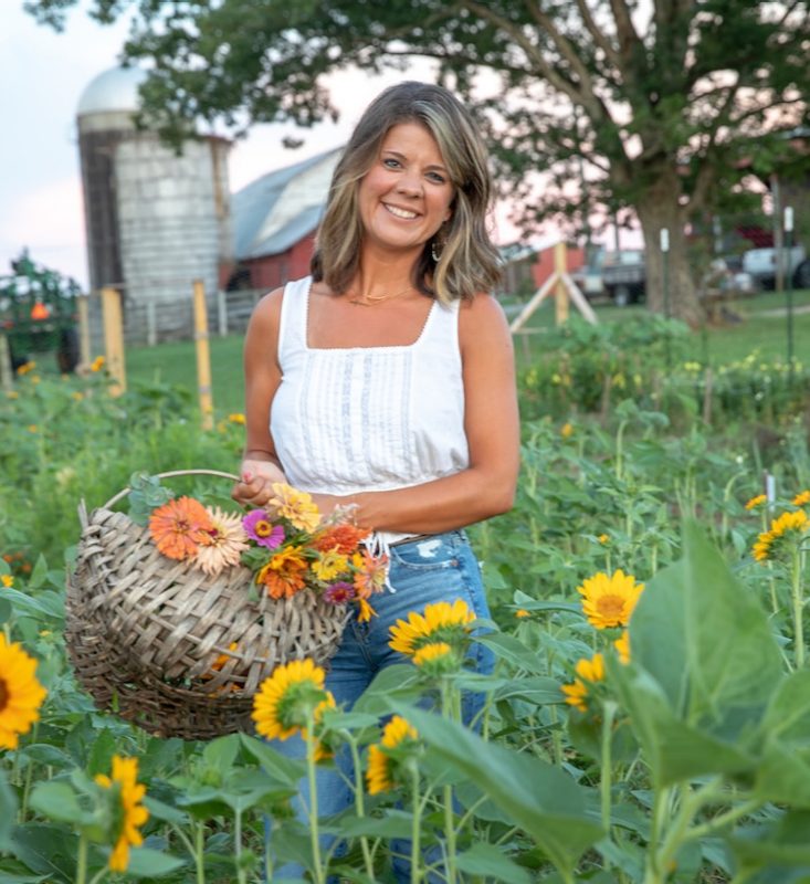 Woman stands in field of sunflowers smiling.
