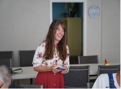 Woman stands in a room and smiles as she speaks to a group.