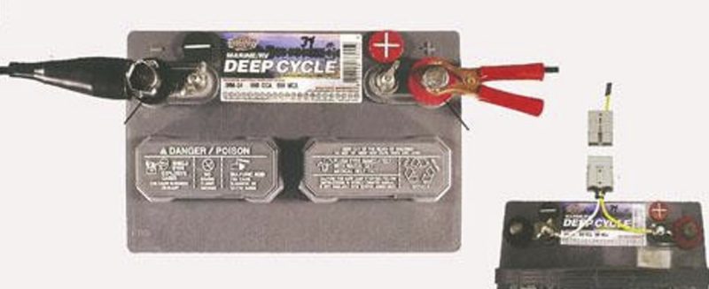 Top view of a battery with black clamp on left and red clamp on right. With light system in bottom right corner.