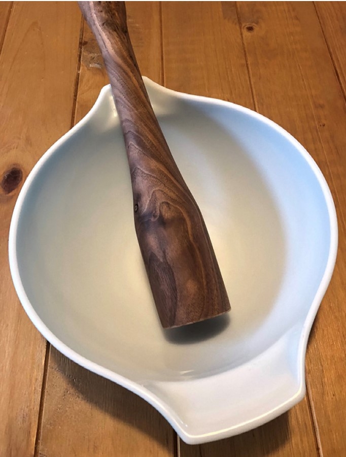 A small, wooden, bat-shaped tool sitting inside a white bowl. 